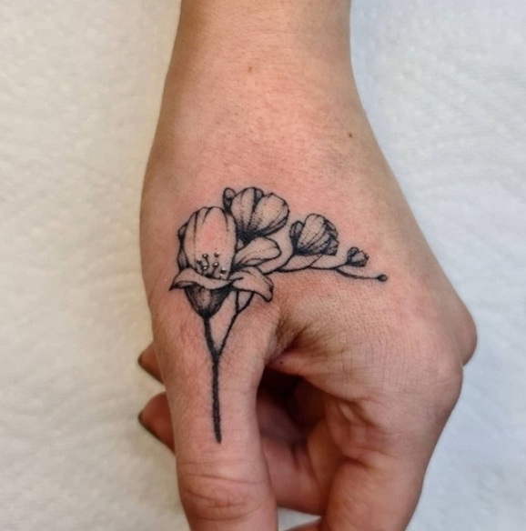 Lille Freesia -tatovering i nærheden af ​​tommelfingeren