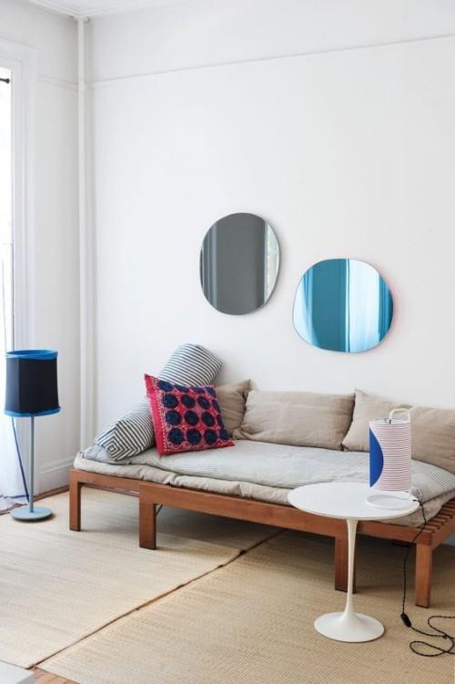 Epäsymmetria sisustuksessa yksinkertaisesti sisustettu olohuone kaksi pyöreää peiliä seinällä sohvatyynyjen lattiavalaisimen yläpuolella