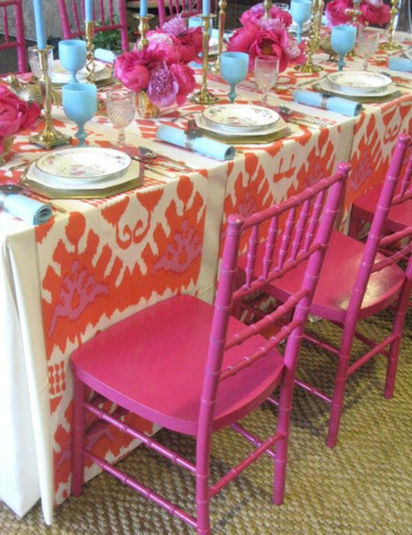 Houkutteleva illallinen, joka on valmistettu posliinista vaaleanpunaisista tuoleista pöytäliina ikat