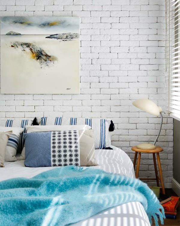 Valkoiseksi maalattu makuuhuoneen tiiliseinä korostaa rauhallista tunnelmaa maalaismainen hohto seinämaalaus jakkara yölamppu