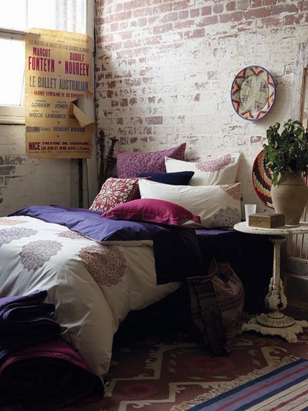 Tiiliseinä makuuhuoneessa, jossa on maalaismaisia ​​yksityiskohtia, niin värikäs koristetyynyillä ja niin houkutteleva