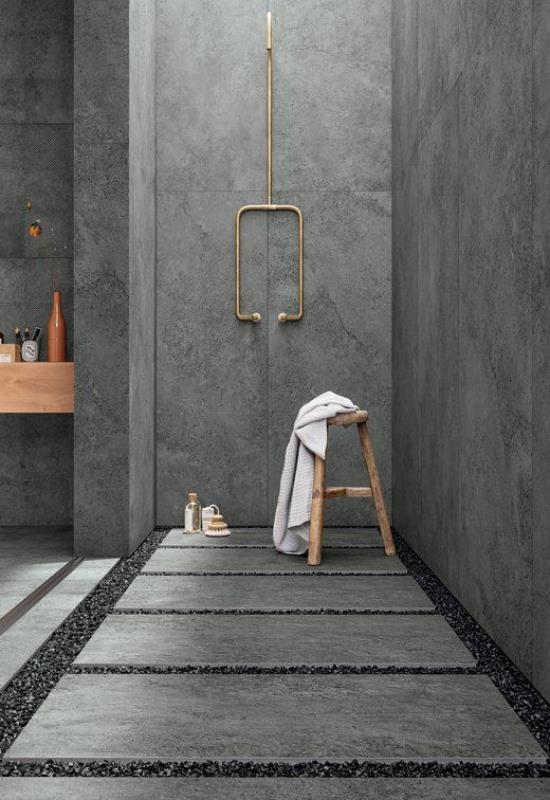 Kylpyhuoneen mallit harmaassa teollisessa betoniseinässä lattialistat, joissa on pienet messinkiset suihkukivet