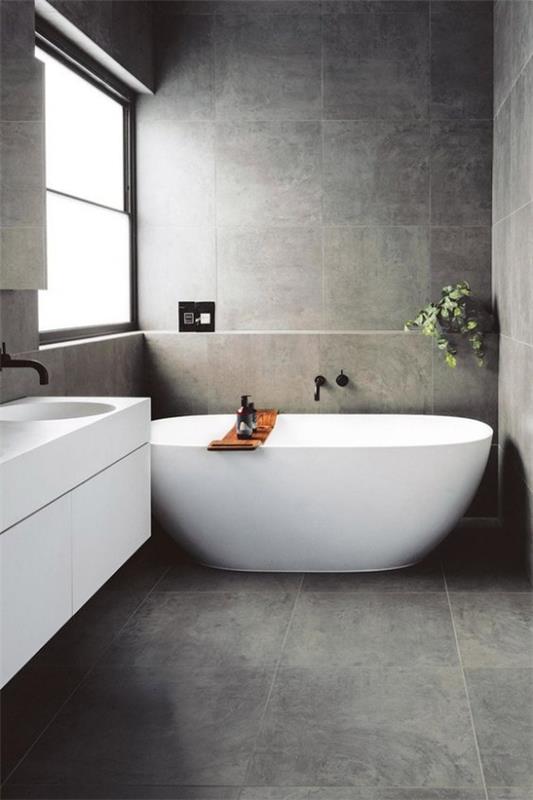 Kylpyhuoneet harmaalla, puhtaalla minimalismilla, harmaat lattia- ja seinälaatat, valkoinen kylpyamme katseenvangitsijana, valkoinen turhamaisuusikkuna oikealla