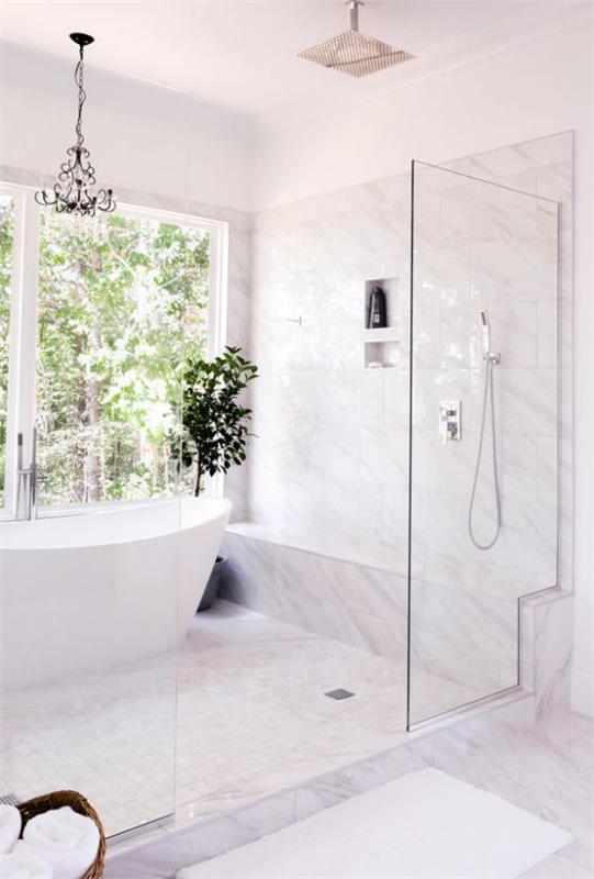 Kylpyhuoneen trendit 2021 iso ikkuna takapihalle valkoinen kylpyamme vaaleat laatat lasiovi