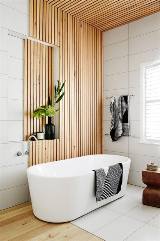 Kylpyhuoneen trendit 2021 tyylikäs kylpyhuoneen muotoilu puupaneelit puulattia valkoinen kylpyamme valkoiset laatat pyyhkeet