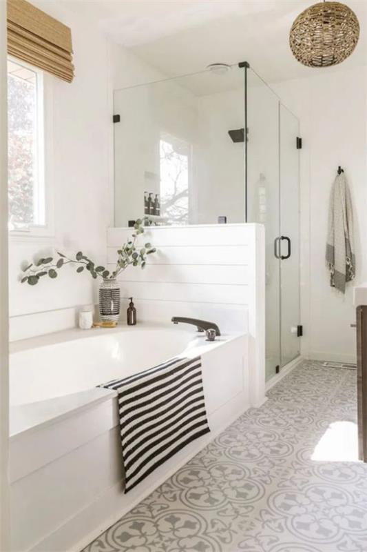 Kylpyhuoneen trendit 2021 valkoinen kylpyamme suihkunurkka lasioven vieressä kevyesti kuvioidut lattialaatat kylpypyyhe mustilla ja valkoisilla raidoilla
