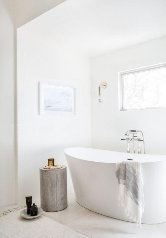 Kylpyhuone kokonaan valkoisessa vapaasti seisovassa kylpyammeen puunrungossa katseenvangitsijana paljon luonnonvaloa