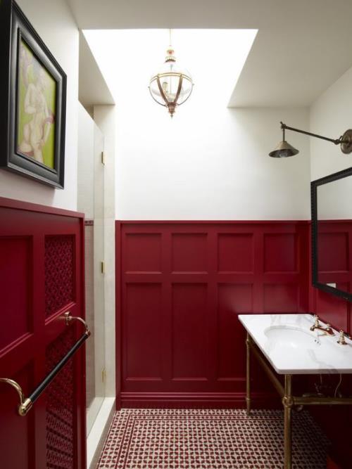 Kylpyhuone punaisella, tummanpunaisella seinäpaneelilla, valkoinen pesuallas oikealla, peili, lamppu vasemmalla, seinämaalaus