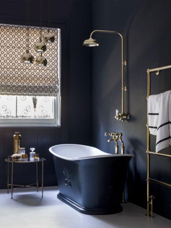 Kylpyhuone mustassa ja kultaisessa vapaasti seisovassa kylpyammeessa tummansinisissä valaisimissa päivänvalossa