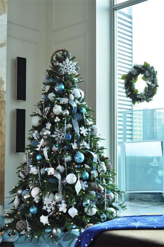 Siniset ja hopeiset joulu- ja uudenvuodenaaton juhlat Joulukuusi, joka on koristeltu ikkunaseppeleen vieressä lasipaneelissa