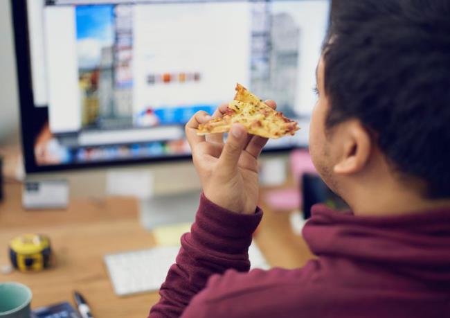 Ruokavalio ansa syö pizzaa tietokoneen edessä töissä huono tapa kotitoimistossa