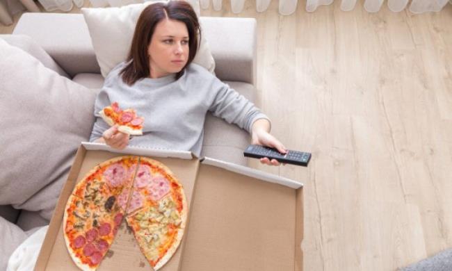Ruokavalio putoaa nuori nainen makaa sohvalla katsellen televisiota syö pizzaa huono tapa