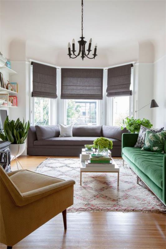 Erkkeri -ikkuna olohuoneessa lisää asuintilaa tummat laskostetut kaihtimet mukavat sohvat nojatuolit matto vihreät huonekasvit
