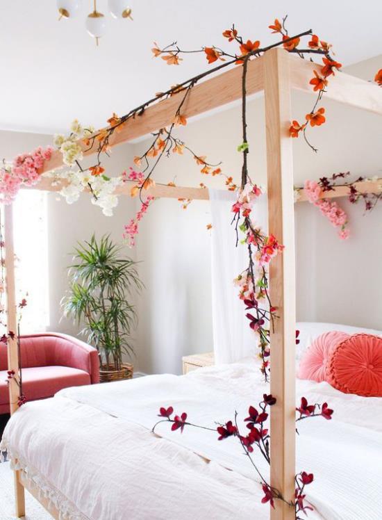 Kevään sisustusideoita makuuhuoneeseen suuri nukkumissänky puukehys koristavat kukkivat oksat romanttinen tunnelma