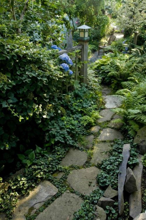 Kivipuutarhapolut, jotka on upotettu vihreään. Puinen lyhty Urban Gardening