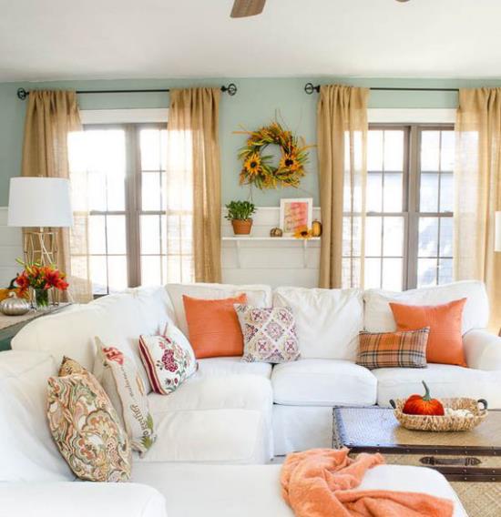 Herbstdeko olohuoneessa valkoinen kulmasohva värikäs heittää tyynyt heittää viltti oranssi syksy seppele seinälle