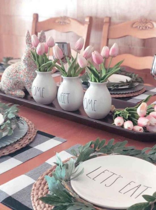 Koristele keittiö kevääksi tarjottimella, jossa on kolme valkoista posliinista maljakoita täynnä vaaleanpunaisia ​​tulppaaneja, juhlallisesti sisustettu ja katettu pöytä