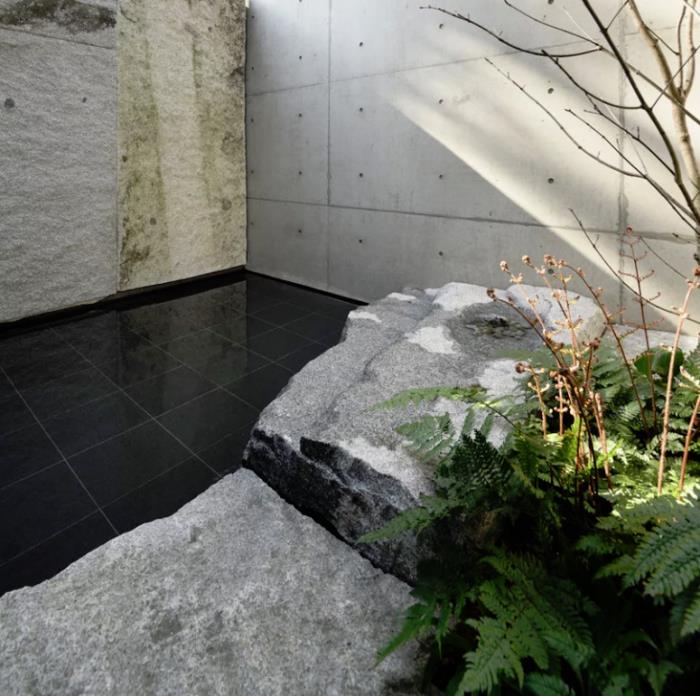 Minimalistinen kivi- ja betonitalo Japanissa sisäpiha sileät mattamustat laatat luonnonkivi suuret laatat puu vihreä saniainen