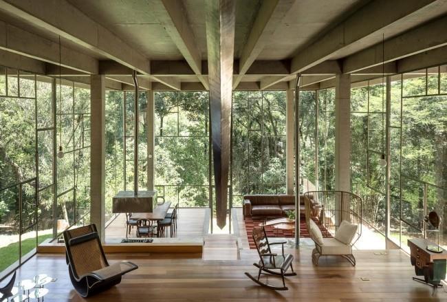 Moderni talo lasista ja betonista sademetsässä, tilava olohuone, korkeat lasiseinät, näkymä ulos