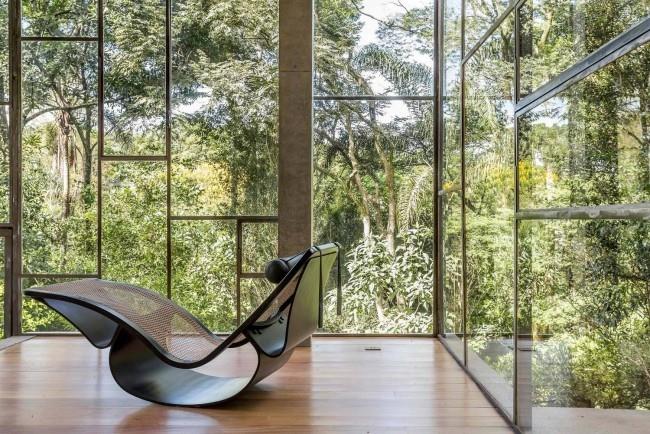 Moderni talo lasista ja betonista sademetsässä luo tyylikkään keinutuolin, jossa on sekoitus modernia ja retro -muotoilua