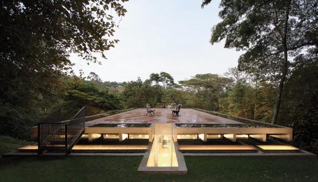 Moderni talo lasista ja betonista sademetsässä, leveä kattoterassi, joka on peitetty säänkestävillä puulevyillä