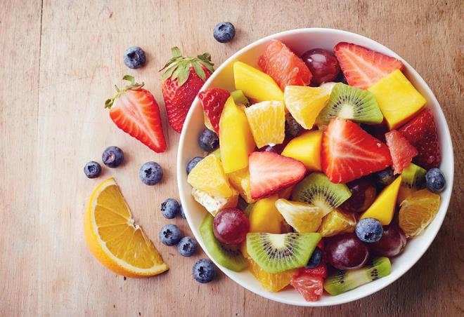 Syö hedelmiä terveellinen laihtuminen rikas hedelmäsalaatti appelsiinit kiivi mansikat mustikat paloiteltuna kulhoon.