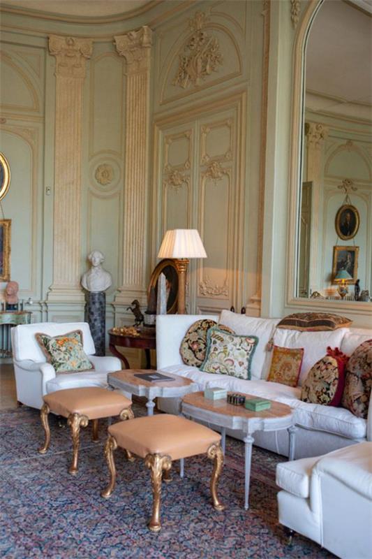 Provence -tyylinen klassinen sisustus olohuoneessa valkoiset istuinkuvioidut heittotyynyt kaksi pientä pöytää kaksi jakkaraa lamppu