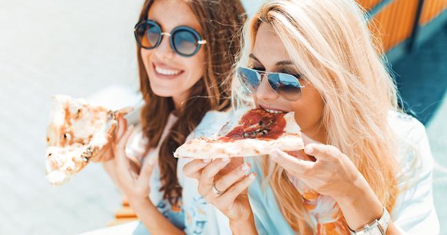 Sääntö kaksi nuorta naista, jotka syövät pizzaa, nauravat iloisesti