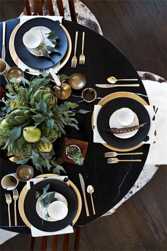 Juhli uudenvuodenaattoa kotona kauniisti järjestetyssä juhlapöydässä, kultaisissa ja mustissa hienoissa ruokailuvälineissä keskellä pöydän maljakkoa vihreillä oksilla