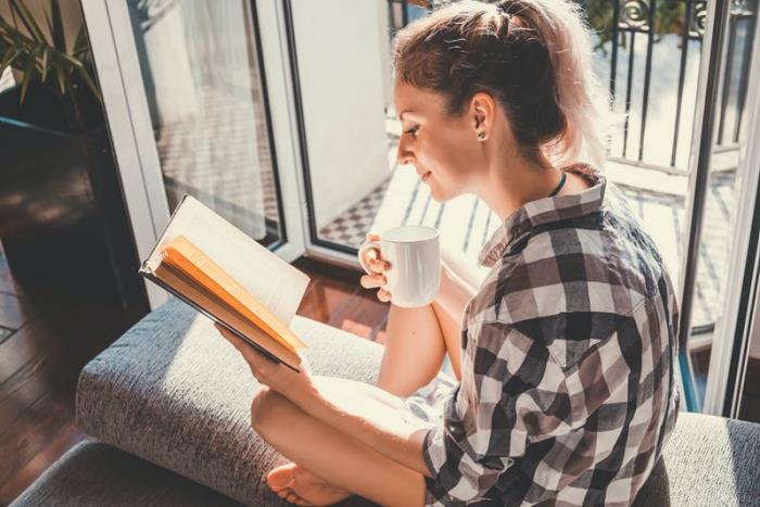 Horoskooppi onnellinen yksin itsenäinen yksinäinen nuori tyttö lukee kirjaa kotona ja juo kahvia