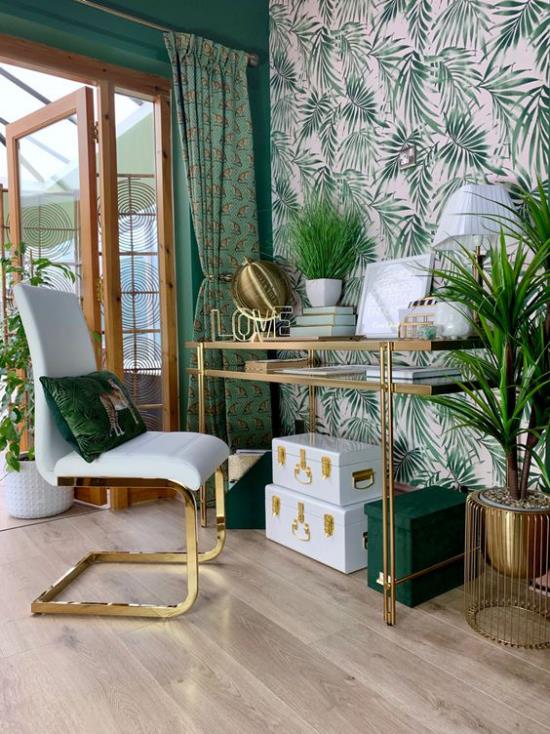 Trooppinen sisustus kotitoimistossa suuri kirkas huone vihreä väri hallitsee kirjoituspöytä nojatuoli aksentti seinä tapetti suuret trooppiset lehdet vihreät ruukkukasvit