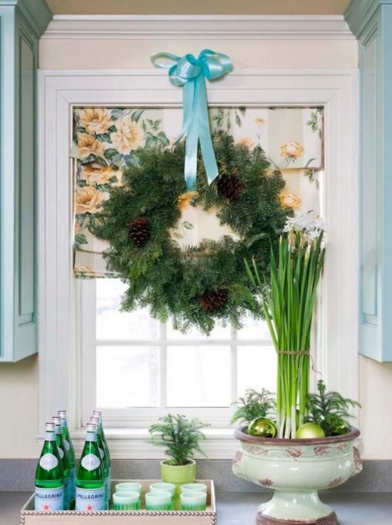 Jouluikkunan koristelu iso seppele kuusen vihreitä käpyjä ja sininen nauha keittiön ikkunassa