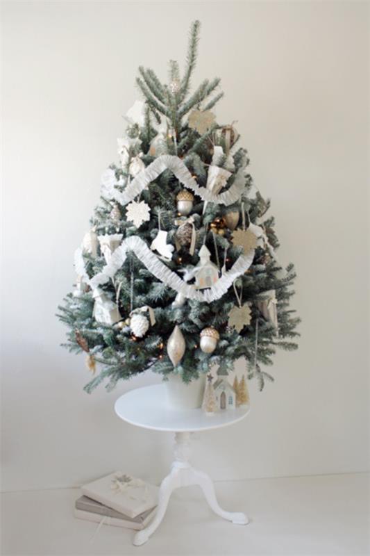 Joulukuusi koristellaan kauniisti valkoisella ja hopealla koristeltu pieni joulukuusi pienelle pyöreälle pöydälle