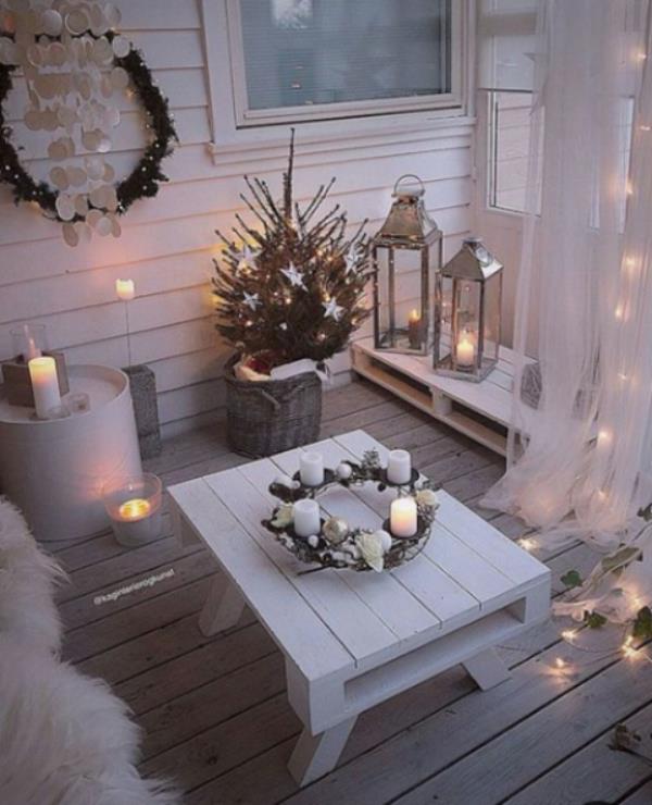 Parvekkeen joulukoristeita valkoisina lukuisat valot ja kynttilät Adventtiseppele matalalla valkoisella pöydällä keskellä