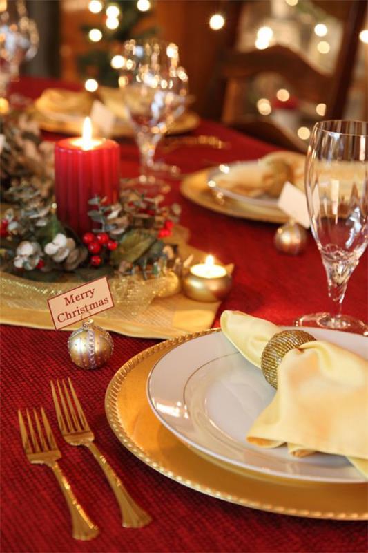 Joulukoristeet punaisella ja kullalla juhlallisesti katettu pöytä punainen pöytäliina hieno posliini kullatut ruokailuvälineet punainen kynttilä
