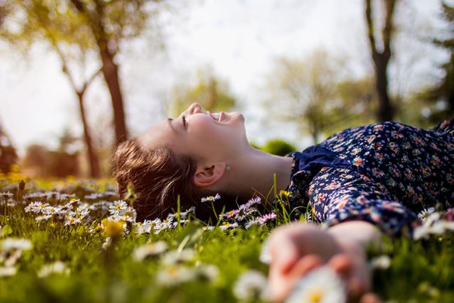 Kansainvälinen naistenpäivä 8. maaliskuuta nuori nainen puistossa makaa nurmikolla auringossa ollessaan onnellinen