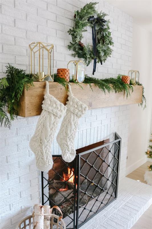 Talvikoristelu olohuoneessa takan ääressä valkoiset joulupukin sukat kuusenvihreä kuin seppele kynttilät lyhdyt seppele seinällä