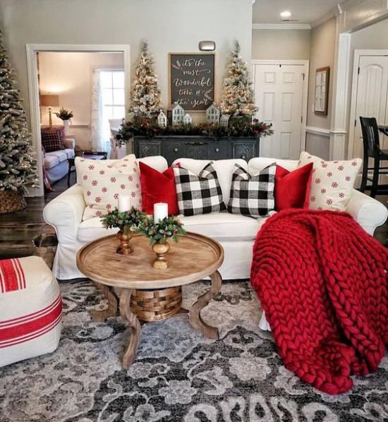 Talvikoristelu olohuoneessa punainen neulottu peitto punainen ja mustavalkoinen ruudullinen heittotyyny valkoinen sohvapeite kuusia taustalla