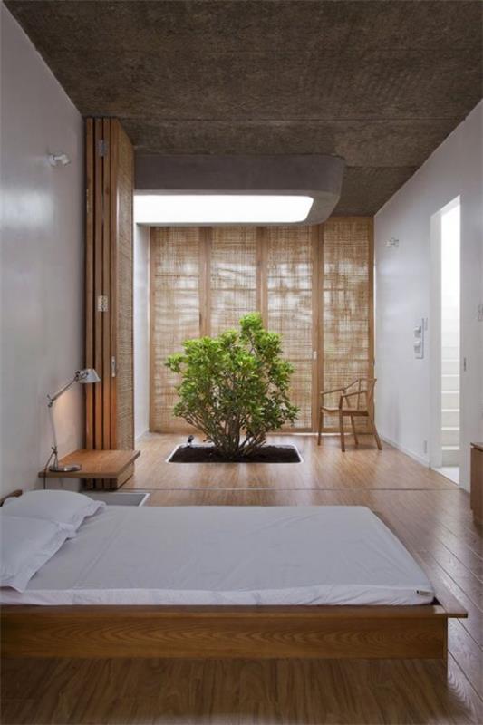 Zen makuuhuone leveä nukkuva sänky kevyt liinavaatteet paljon puuta iso tummennettu ikkuna pieni puu vihreä huomautus