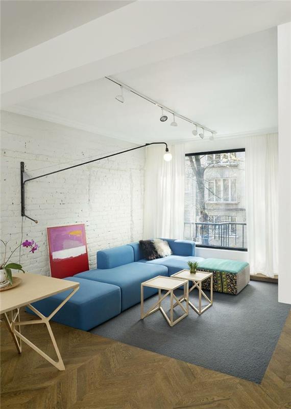sininen sohva vaaleansininen kulmasohva harmaa matto tiiliseinä sivupöydät