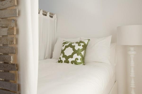 yhden huoneen huoneisto, jossa on lumivalkoiset vuodevaatteet ja oliivinvihreät kuviotyynyt