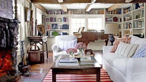 kodikas maalaistyylinen olohuone paljon puuta valkoisia huonekaluja raidallinen matto palkit kirjahylly