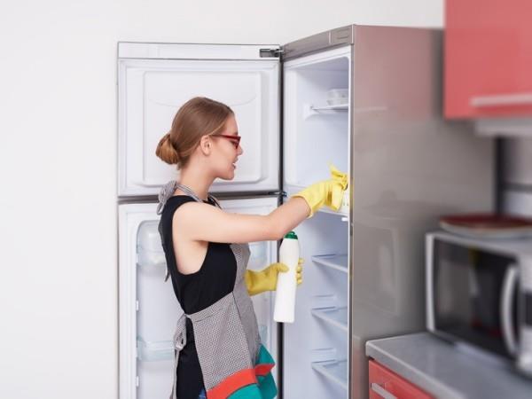 sivukuva naisesta, joka puhdistaa jääkaapin