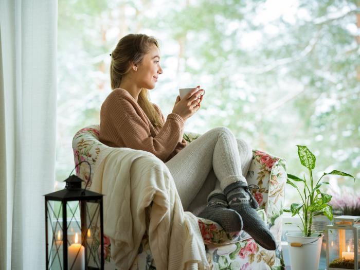 terve ja onnellinen talvella pysy viihtyisänä kotona nainen nojatuolissa juo teetä rentoudu vihreä kasvi sen vieressä