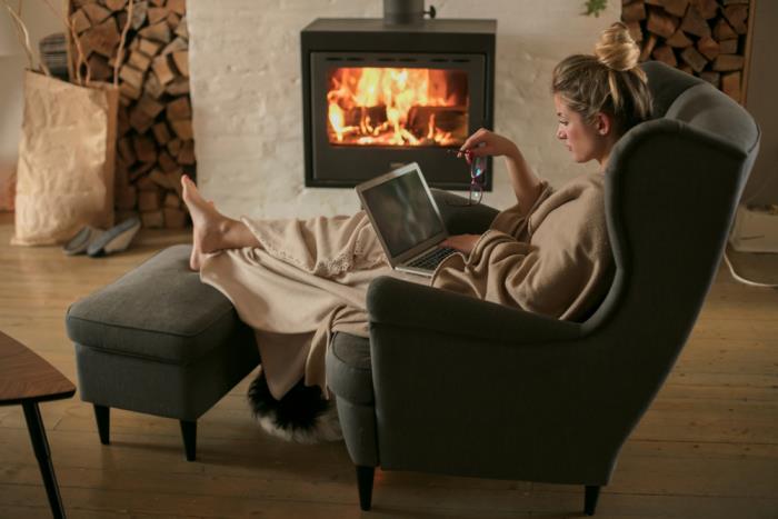 terve ja onnellinen talvella nuori nainen nojatuolissa palavan takan edessä kirja kädessään polttopuut lämmin kodikas huoneilmapiiri