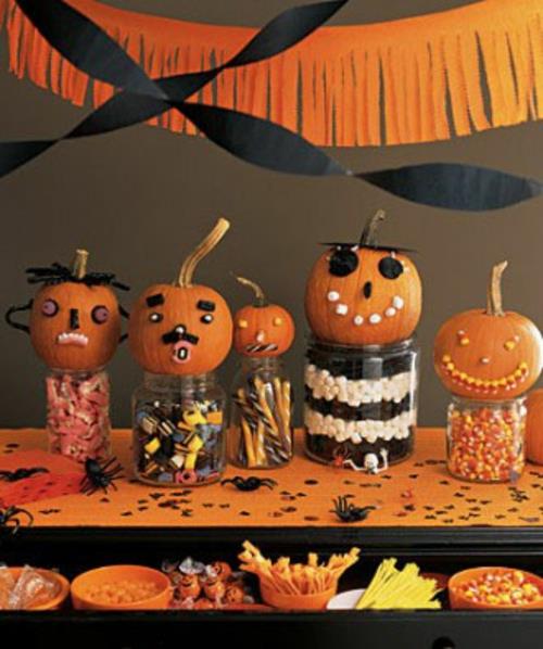 halloween -pöydän koristepurkit, joissa on karkkia ja mini -kurpitsat, joissa on kasvot