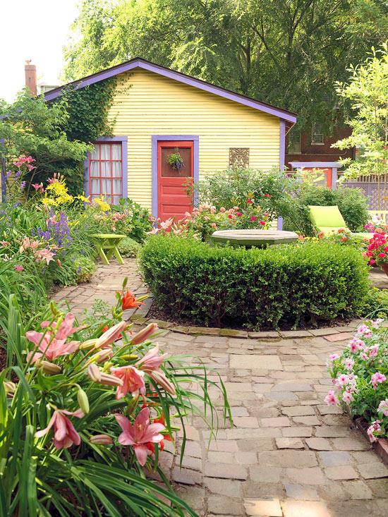 Vaaleanpunaiset liljat ja pelargoniumit kukkapenkin reunalla tuovat puutarhaan enemmän väriä. Kaunis näkymä mökkipuutarhaan