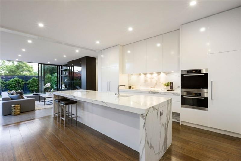 moderni keittiö, jossa on marmorinen keittiösaari ja valkoiset keittiökaapit