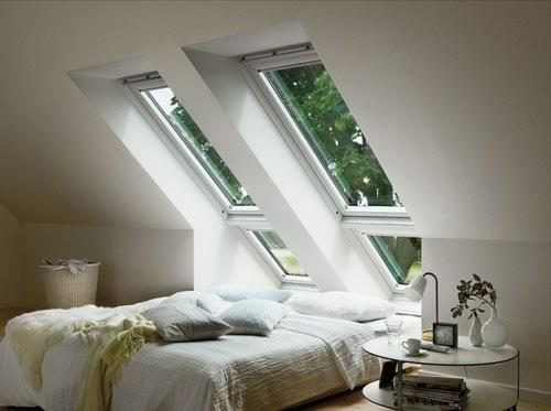 kalteva ikkuna suunnittelee kattohuoneen valkoisen makuuhuoneen sängyn vieressä olevan pöydän