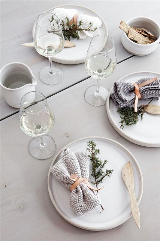 uudenvuodenaaton pöytäkoriste valkoisilla lautasilla ja kuusenvihreällä